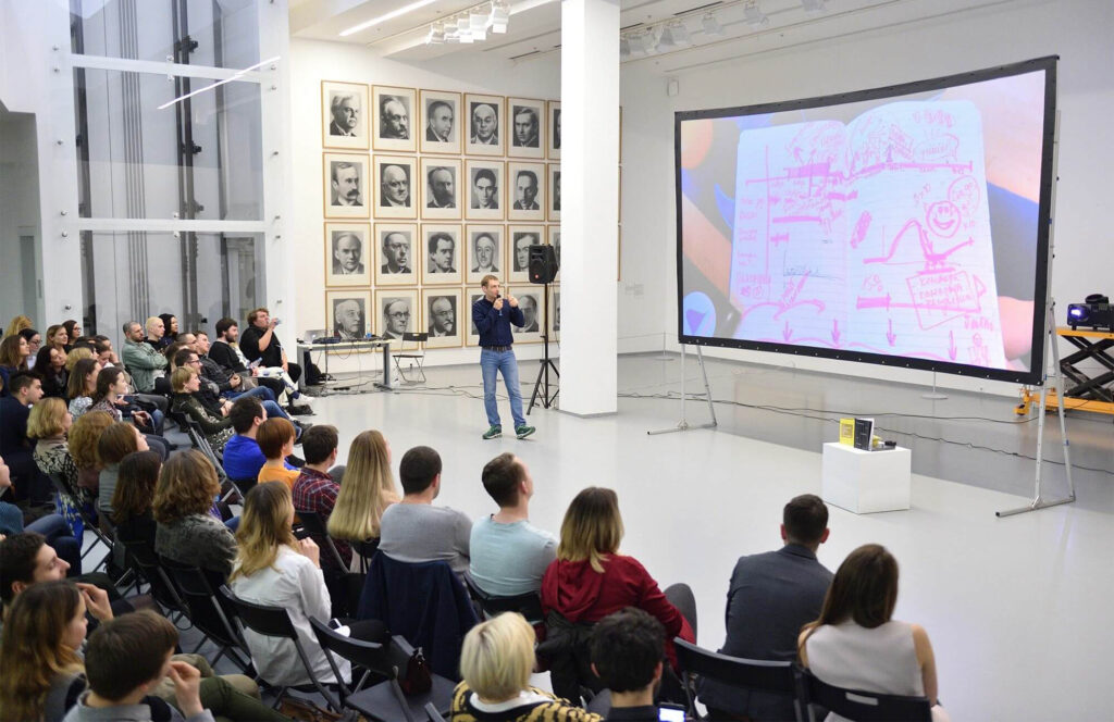 Group of people sitting in a large white room during a presentation